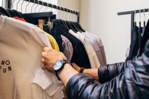 A picture of a buyer looking through a clothing rack at a store.