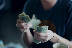 A picture of a person counting dollar bills, showing how affordable reputation management can be with BRANDefenders.